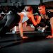 A couple collaborates in a partnered push-up workout session at the gym, symbolizing fitness and teamwork.